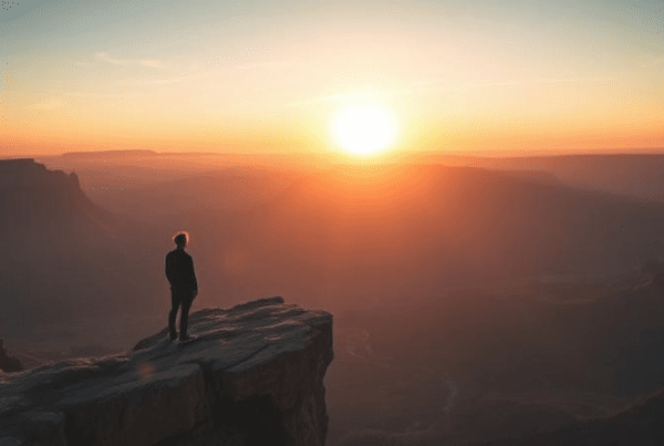 Person standing at a cliff's edge during sunrise, symbolizing self-discovery and purpose.